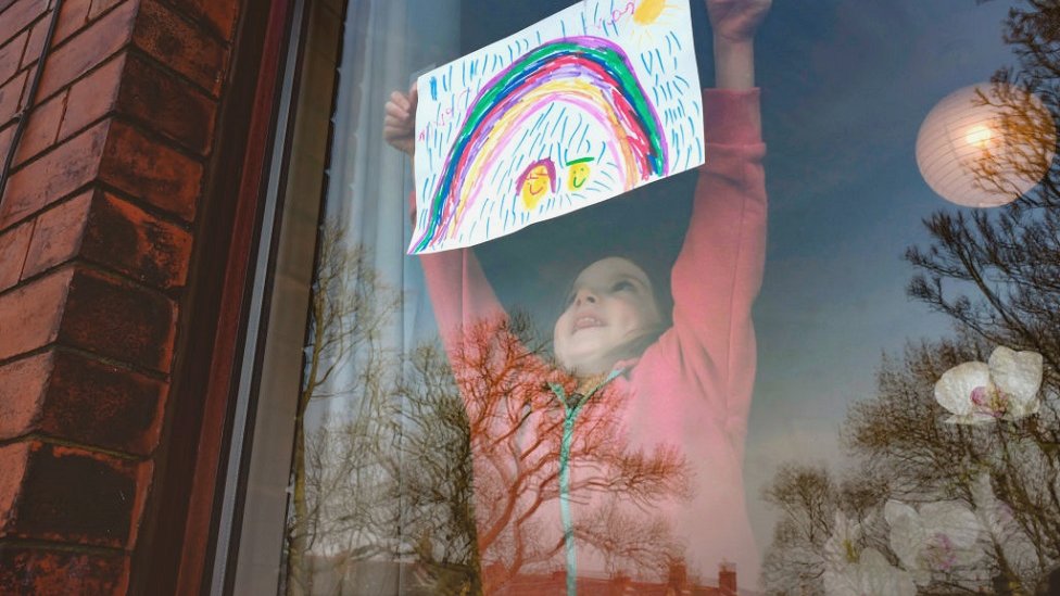 Una niña cuelga un arcoíris dibujado en la ventana.