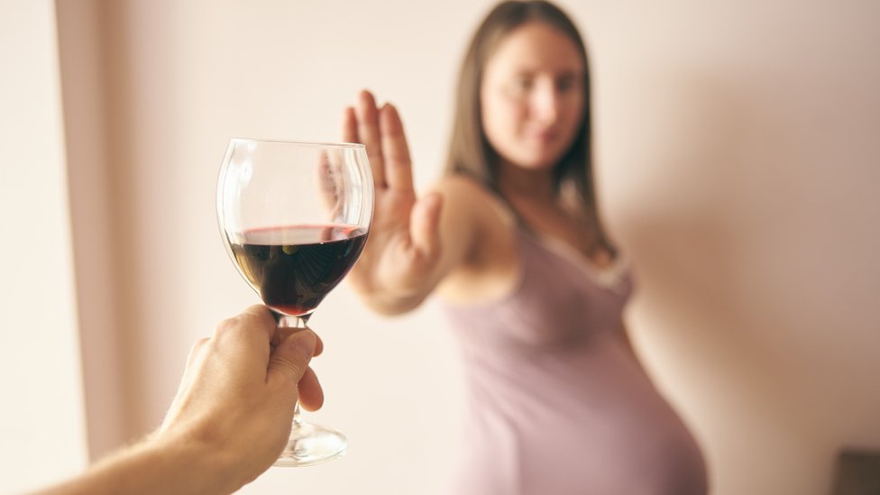 Una mujer embarazada rechaza una copa de vino.