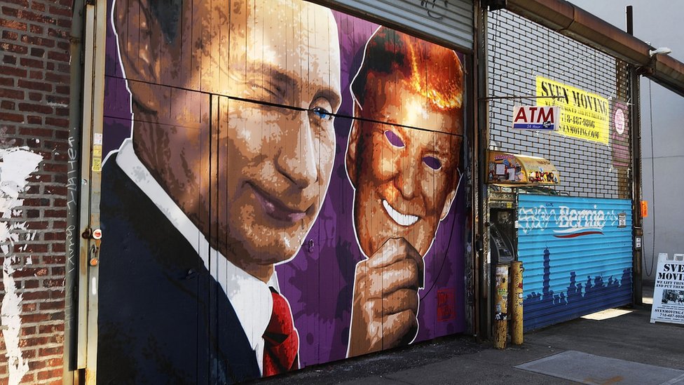 Фреска с изображением подмигивающего Владимира Путина, снимающего маску Дональда Трампа, нарисована на витрине в Бруклине, Нью-Йорк