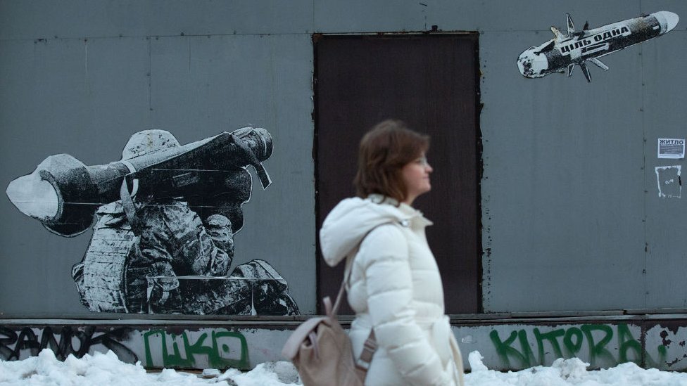 A woman walks in front of the graffiti depicting a Ukrainian serviceman making a shot with a US-made Javelin portable anti-tank