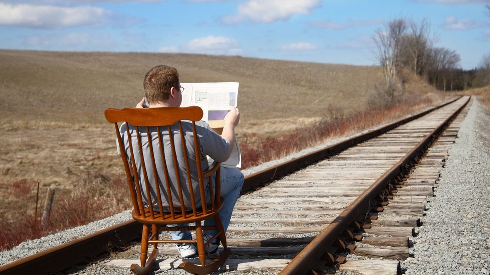 Hombre lee el periódico en las vías del tren