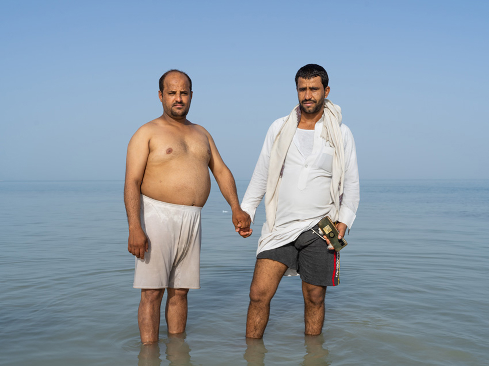 Dos hombres se toman de la mano mientras están parados en el mar.