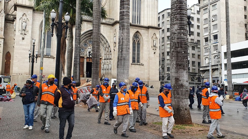 Equipes da prefeitura são protegidas por guardas municipais enquanto fazem limpeza na praça da Sé
