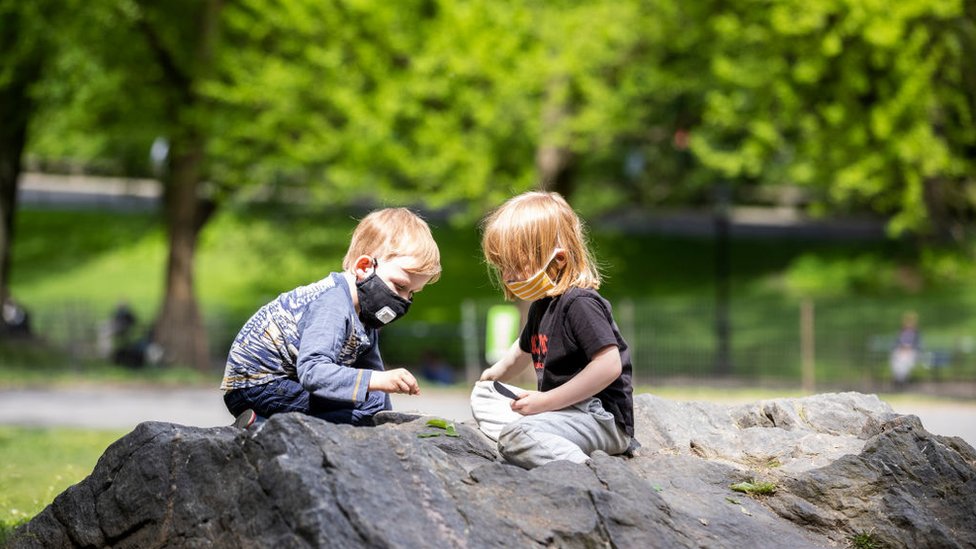 В выходные Дня поминовения двое детей в масках (средствах индивидуальной защиты) сидят на камнях и играют с листьями в Центральном парке