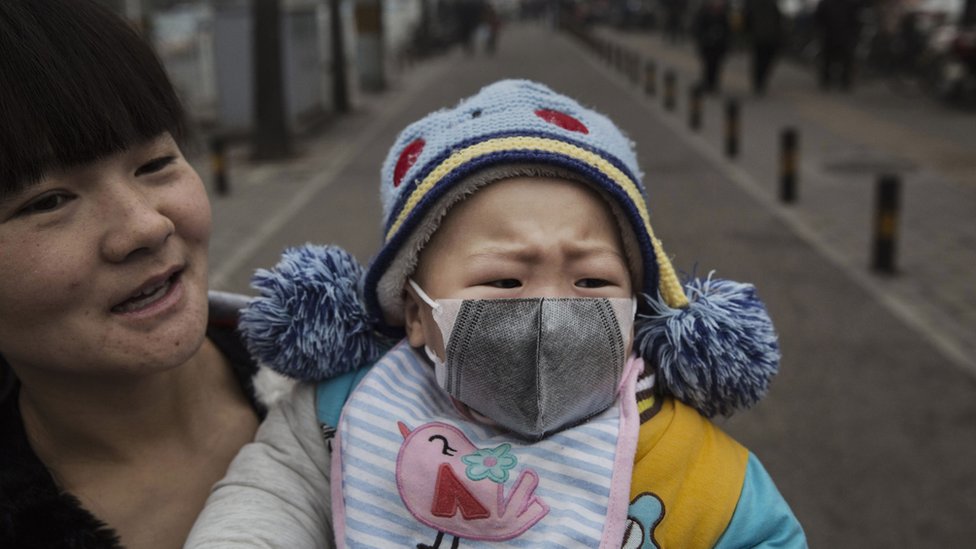 Китайская девушка носит маску, когда ее держит мать в день сильного смога в Пекине, Китай