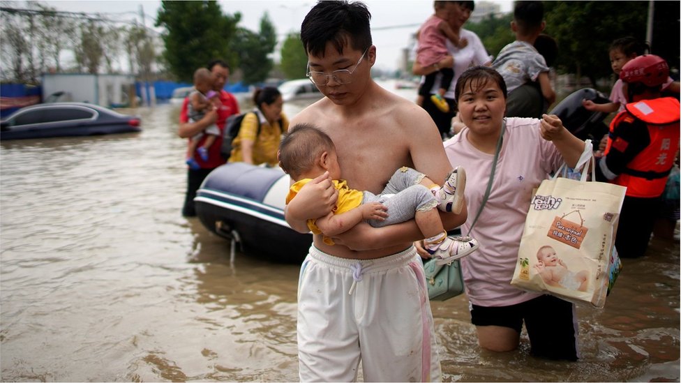 A man holding a baby wades through a flooded road following heavy rainfall in Zhengzhou, Henan province, China July 22, 2021