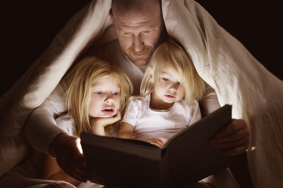 Un padre le lee a sus dos niñas