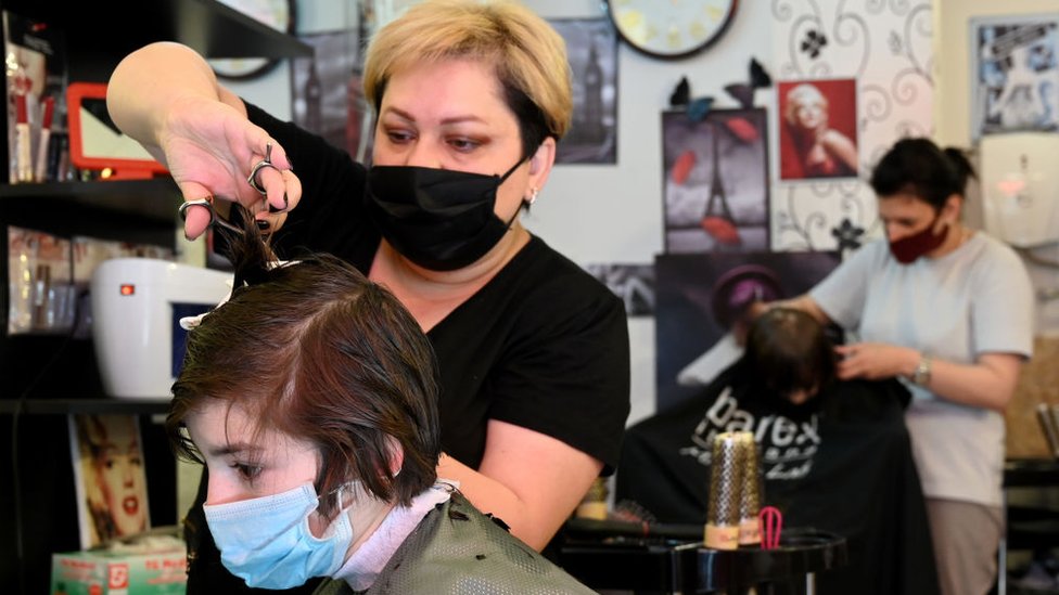 Парикмахер в маске для лица стрижет волосы клиентке в парикмахерской в ??Грузии