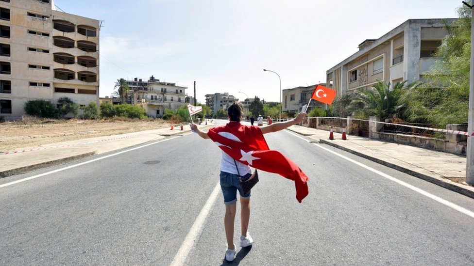 Женщина идет с флагами турок и киприотов в руках внутри территории, огороженной турецкими военными с 1974 года