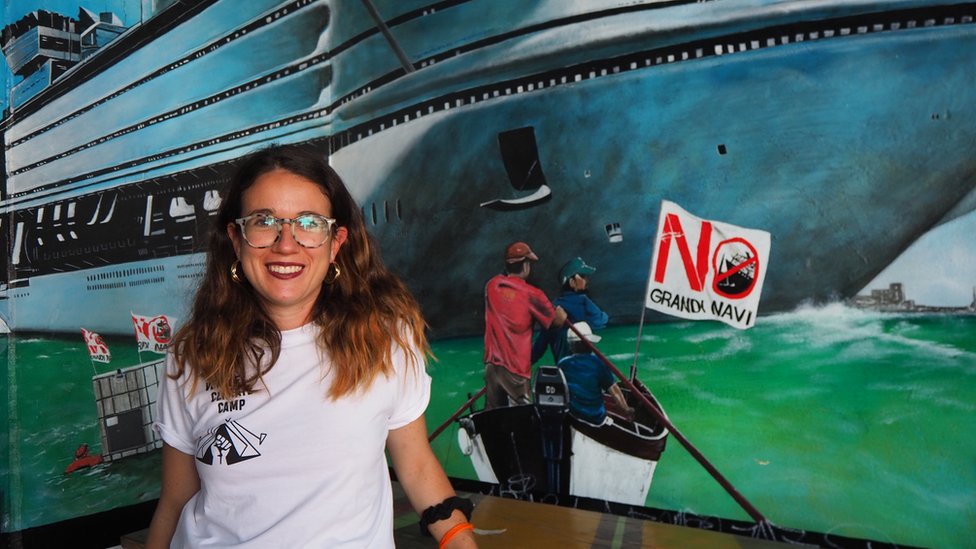Environmental activist Sofia Demasi in front of a mural of a cruise ship and a small boat with a 'No Big ships' logo