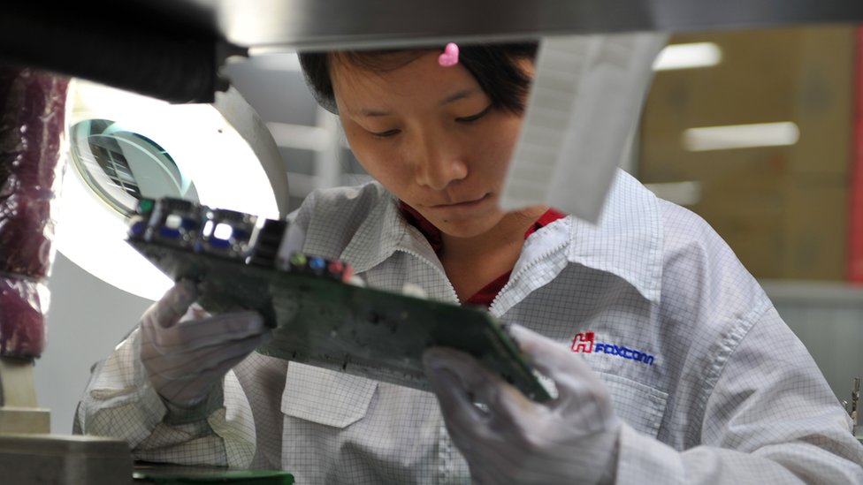 Рабочий осматривает материнскую плату на заводской линии на заводе Foxconn в Шензене на 26 мая 2010 г.