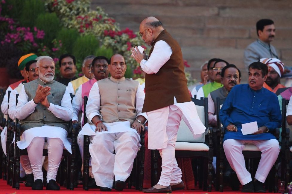 Амит Шах (C) жестикулирует в сторону недавно приведенного к присяге премьер-министра Индии Нарендры Моди (слева) перед тем, как принять присягу в качестве министра в доме президента в Нью-Дели 30 мая 2019 года.