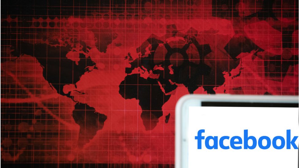 Логотип гиганта социальных сетей Facebook виден на экране телефона рядом с красной иллюстрацией мирового и финансового рынков.