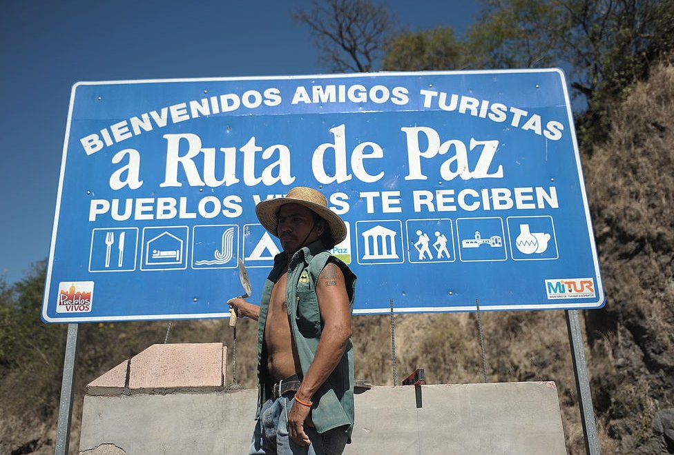 Un trabajador frente a un cartel de la "ruta de la paz" en Osicala, en Morazán.