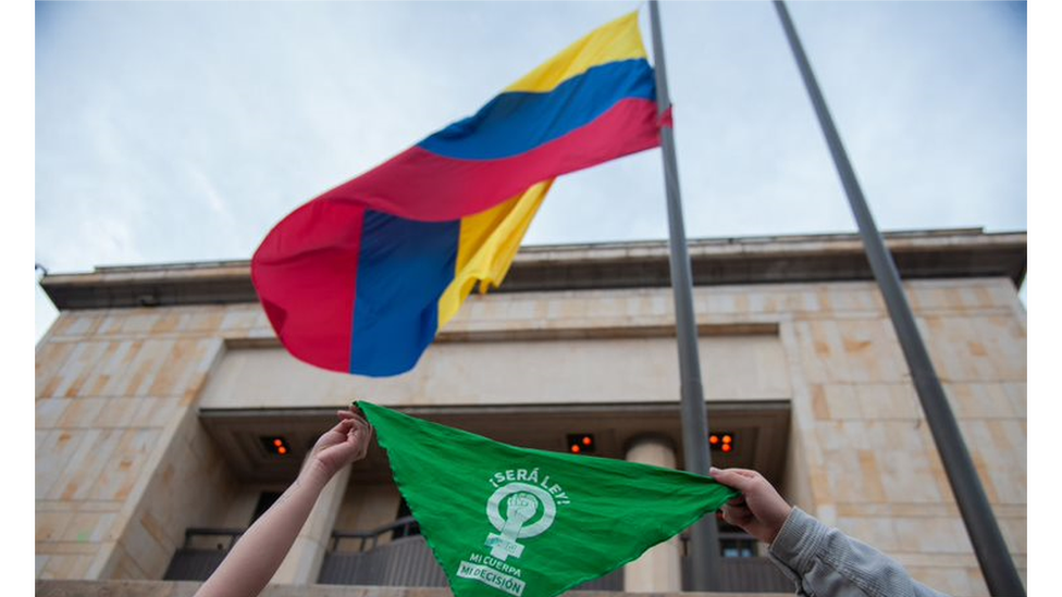 A "green" wave bandana is waved in front of a Colombian flag outside the Constitutional Court building