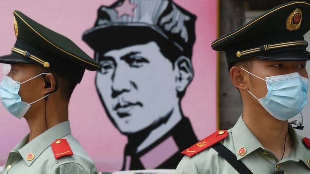 Policiais chineses usando máscaras em frente a uma imagem de um homem usando um boné com uma estrela vermelha