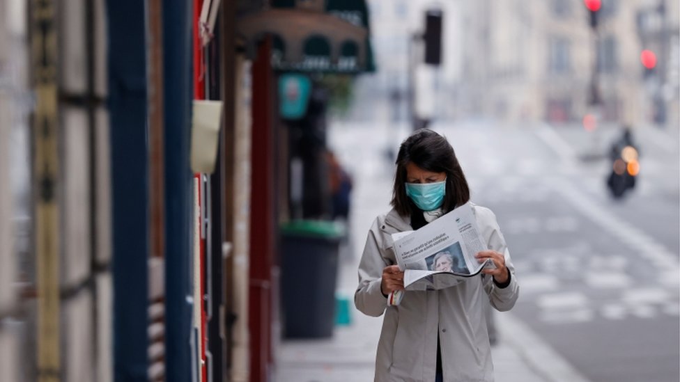 žena s maskom čita novine na ulici