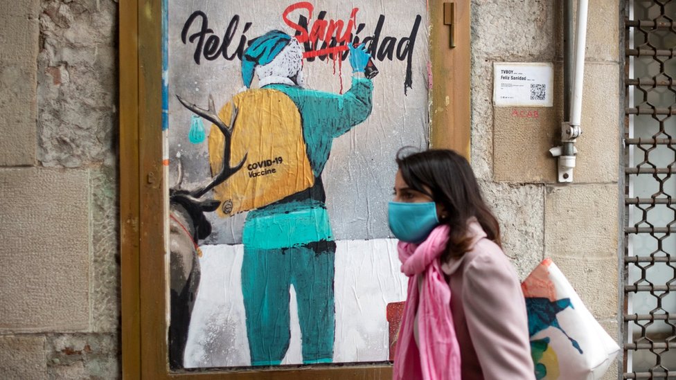 Un mujer pasa frente a un grafiti que alude a una Navidad con coronavirus