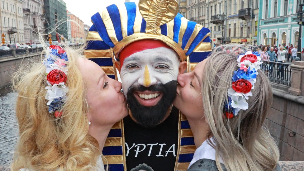 две русские женщины целуют фаната настольного футбола в щеку