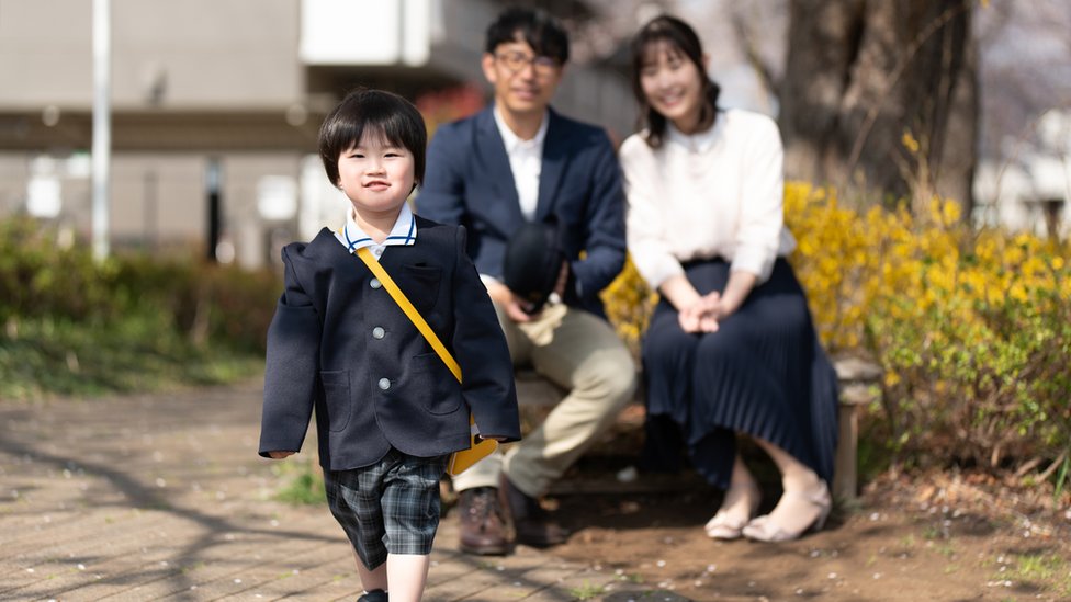 Una niña japonesa se dirige a la escuela mientras sus padres la observan