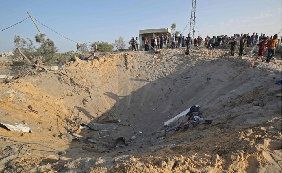 Палестинцы собираются вокруг кратера после израильского авиаудара по Дейр-эль-Балаху в Газе