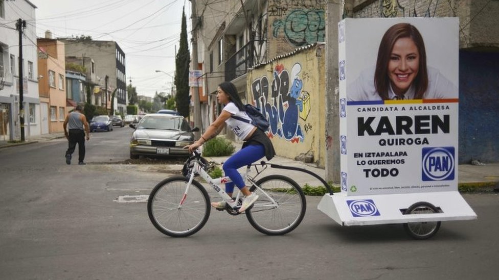 Una joven arrastra un anuncio político en una bicicleta
