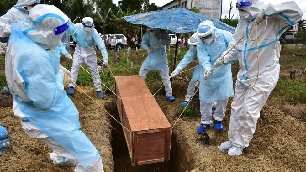穿著個人防護裝備的工作人員在泰國那拉提瓦府的一個墓地埋葬一名死於新冠的民防志願者（2022年2月24日）