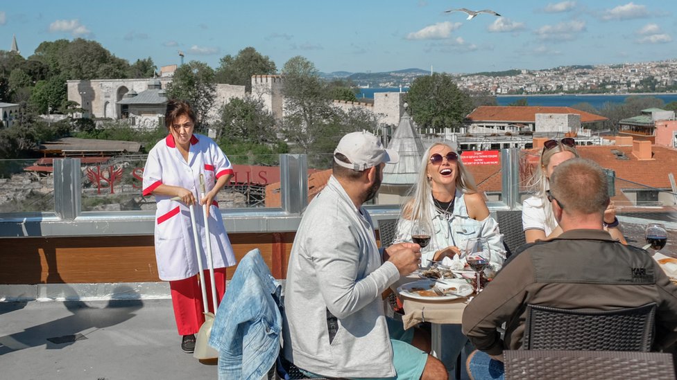 A group of tourists enjoy a meal in Istanbul while a cleaner is standing nearby
