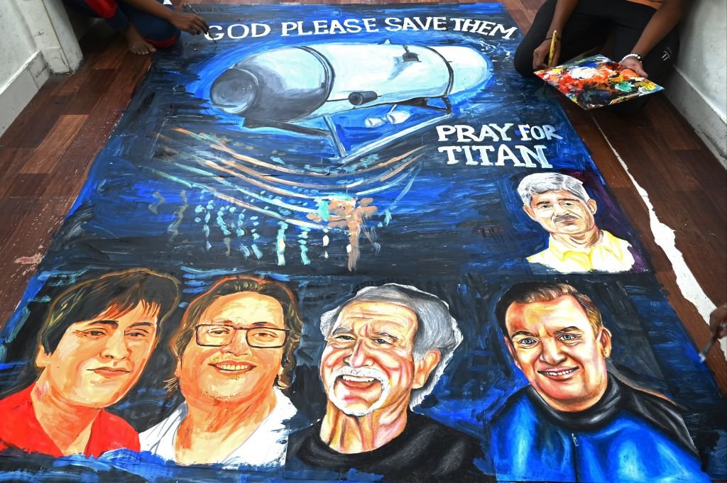 Estudiantes ponen los toques finales a una pintura con las caras de los cinco tripulantes a bordo del Titán con un texto que lee: "Dios los salve".