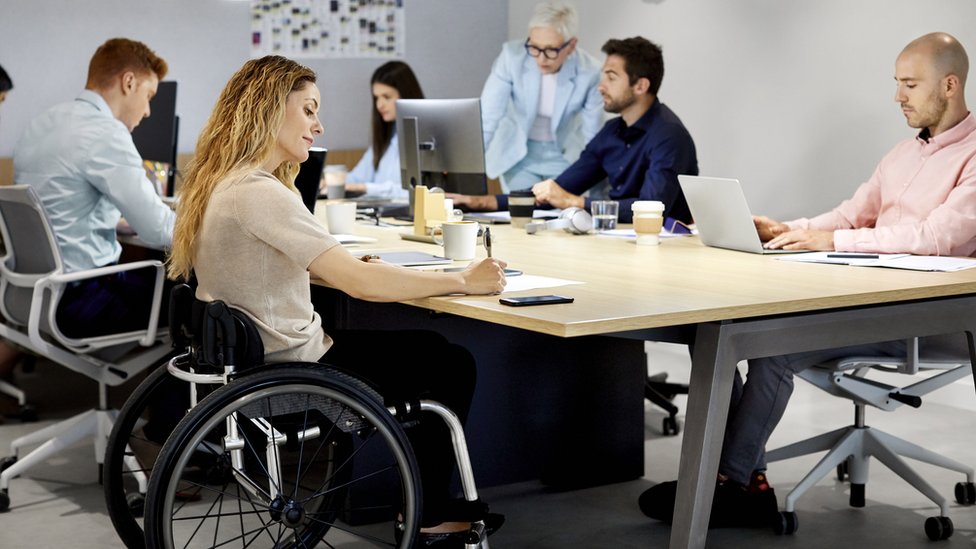 Молодая женщина в инвалидной коляске делает заметки на встрече