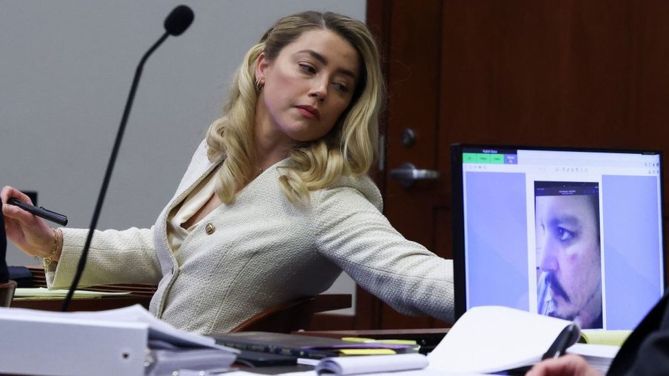 Actress Amber Heard listens to her ex-husband Johnny Depp, as a picture of an injury to his face is seen on a screen, during his defamation trial against her at the Fairfax County Circuit Courthouse in Fairfax, Virginia, April 20, 2022