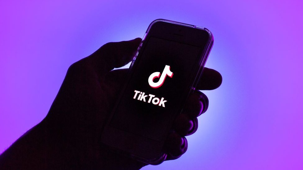 An illustration of a hand holding a phone showing the TikTok logo