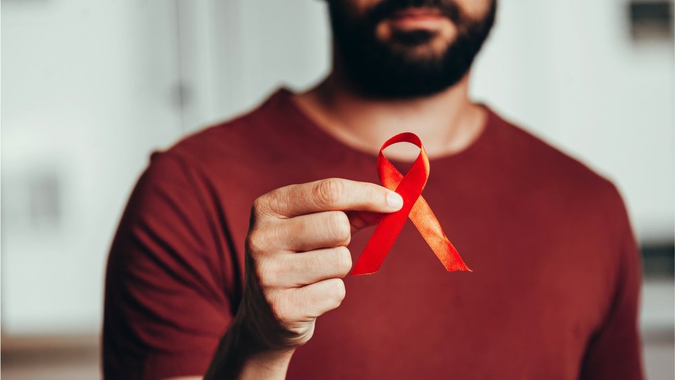 A man holding a red ribbon for HIV illness awareness (stock photo)