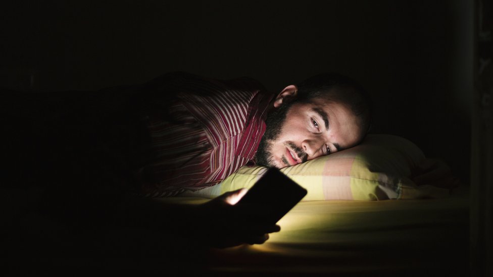 Hombre en la cama, mirando el celular durante la noche
