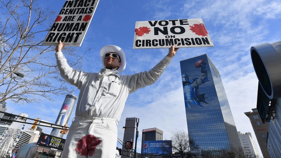 Hombre llevando una pancarta en protesta contra la circuncisión.
