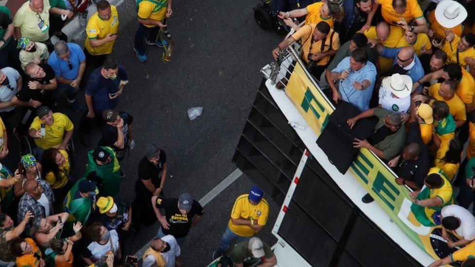 Foto aérea mostra Bolsonaro falando no microfone em cima de trio elétrico, e dezenas de apoiadores em volta e na rua