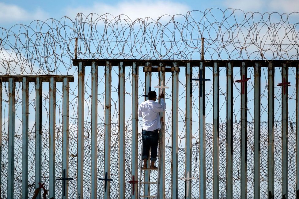 Josué Serrano, un migrante deportado, pone una cruz en la valla fronteriza en Tijuana.