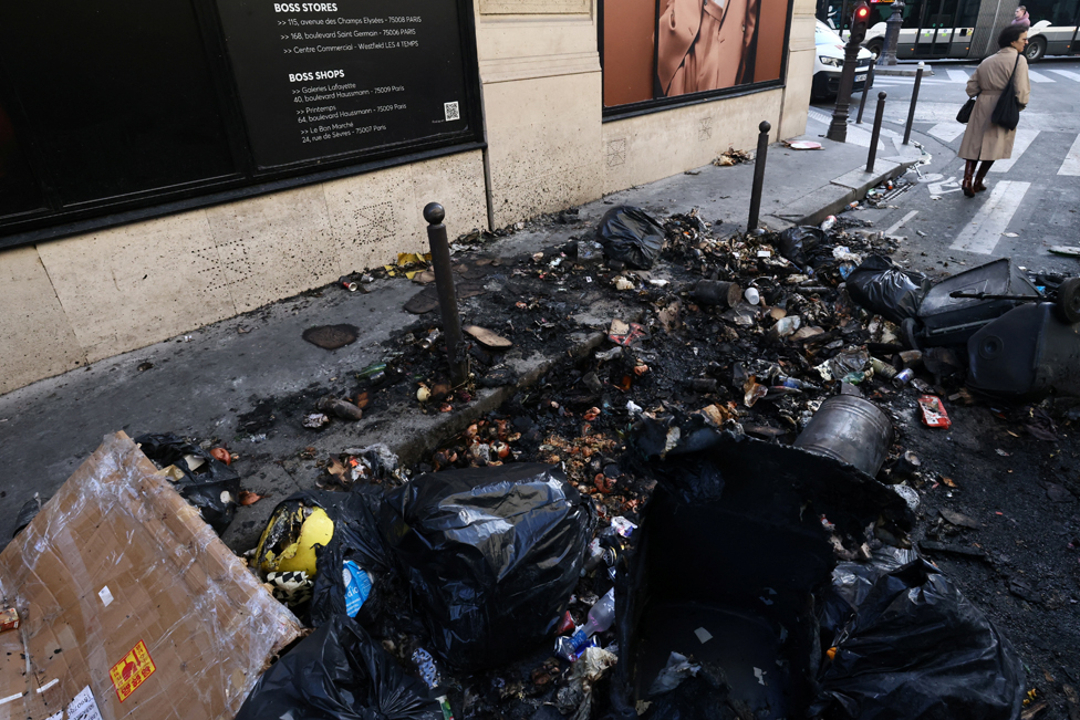A woman stands next to burnt rubbish in a street the day after clashes during protests over French government's pension reform in Paris, France, March 24, 2023.