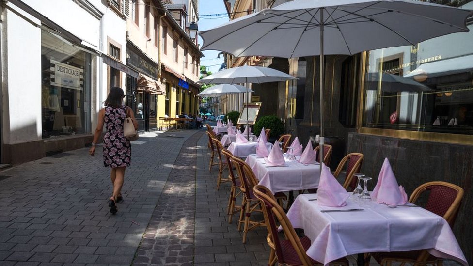 A woman in a dress walks past an empty restaurant in Strasbourg, eastern France, in June 2020
