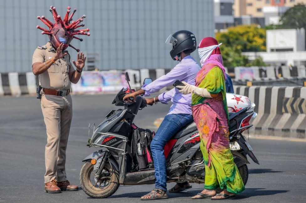 Инспектор полиции Раджеш Бабу (слева) в шлеме, посвященном коронавирусу, разговаривает с автомобилистами во время введенной правительством общенациональной блокировки в качестве превентивной меры против коронавируса COVID-19 в Ченнаи 28 марта 2020 г.