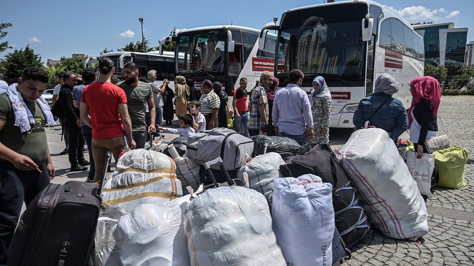 Семьи сирийских беженцев вместе с другими волонтерами ждут, чтобы сесть на автобусы, возвращающиеся в соседнюю Сирию в районе Эсеньюрт в Стамбуле