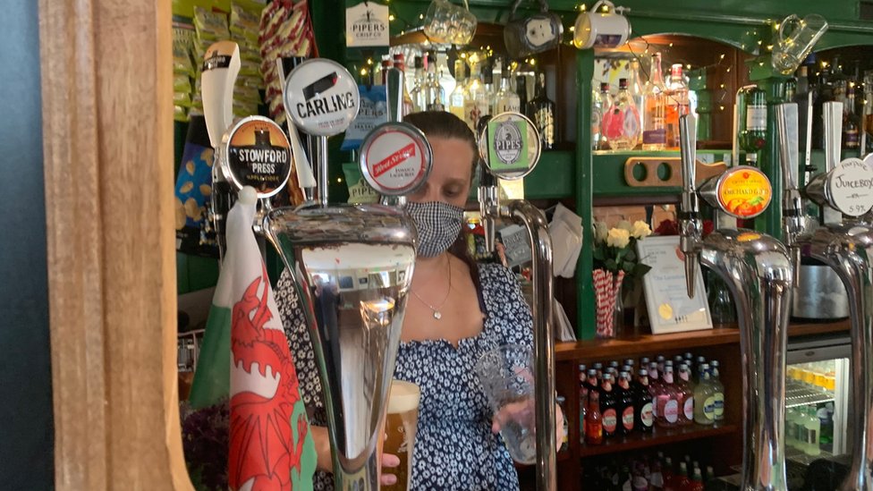 Женщина в маске подает напитки за барной стойкой паба The Landsdowne в Кардиффе