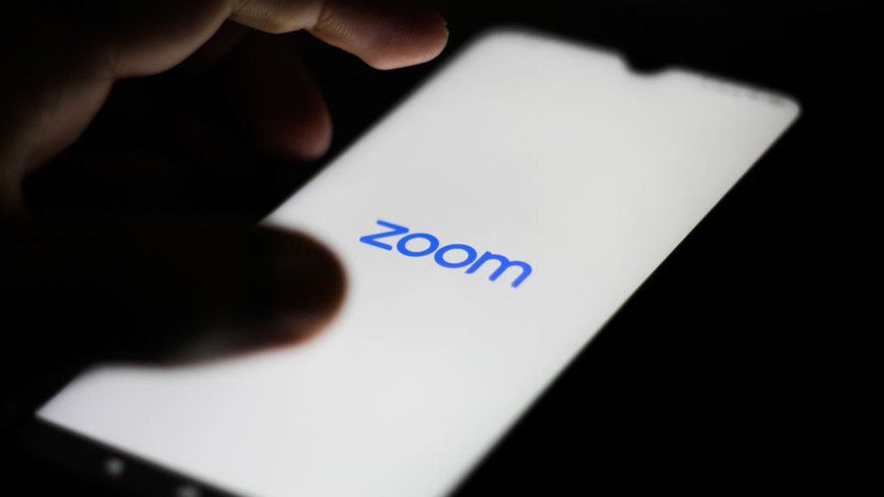 Логотип Zoom показан на смартфоне крупным планом с парящей рукой рядом