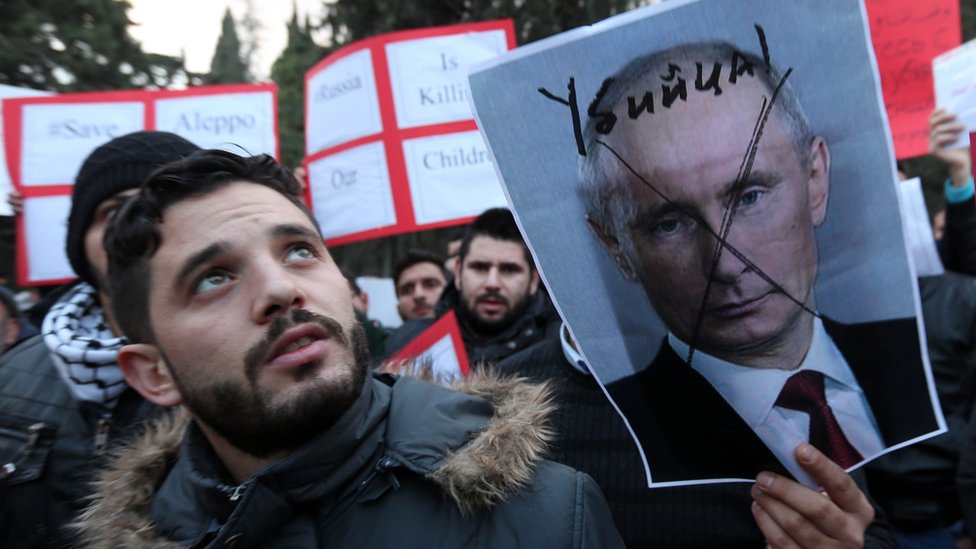 Жители Иордании и сирийцы, живущие в Иордании, держат искаженную фотографию президента России Владимира Путина во время акции протеста перед посольством России в Аммане, Иордания