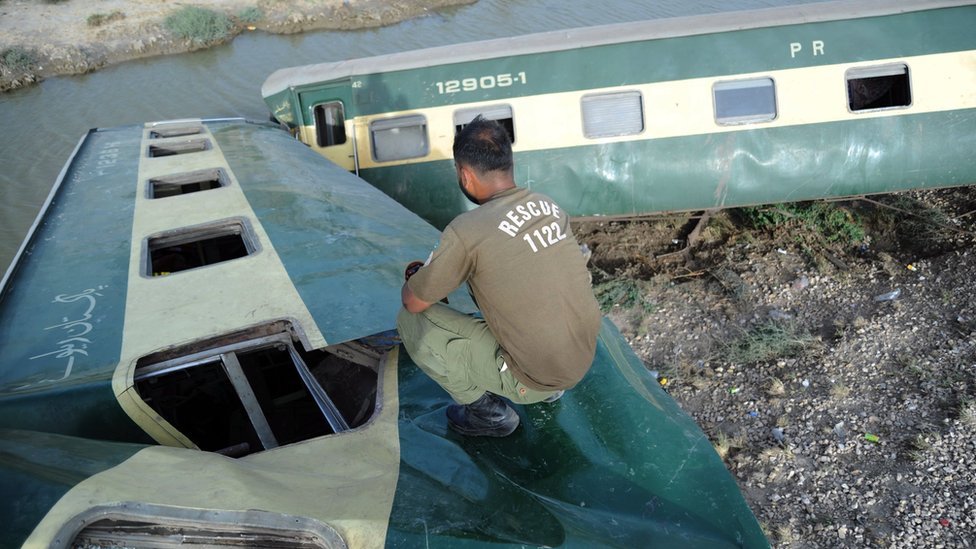 巴基斯坦信德省納瓦布沙阿客運火車出軌事故現場救援人員在扭曲的車廂殘骸中攀爬（6/8/2023）