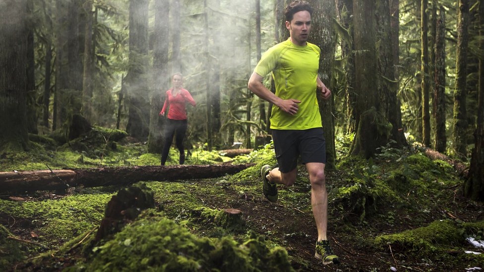 Un hombre corriendo por el bosque con una llamativa camiseta amarilla