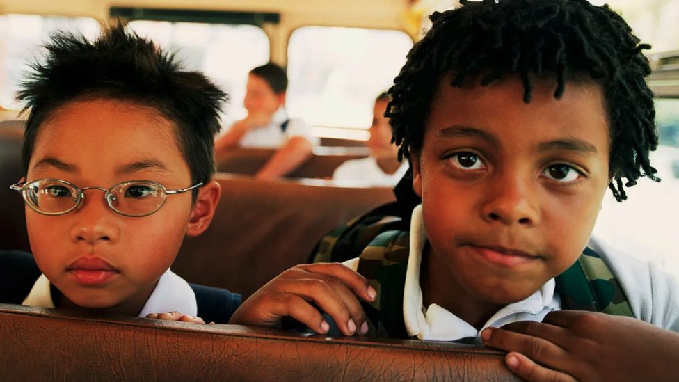 Two children sitting on a bus with two other children sitting behind them