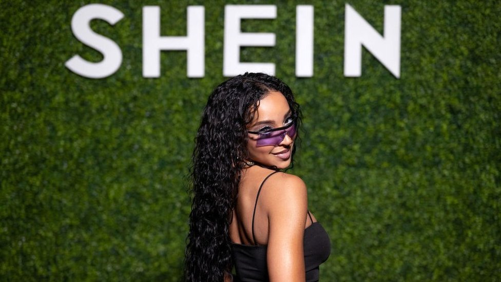 Singer Tinashe poses in front of a Shein sign.