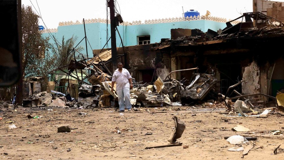 رجل يسير بالقرب من مبان متضررة في السوق المركزي خلال اشتباكات بين الجيش السوداني وقوات الدعم السريع في شمال الخرطوم