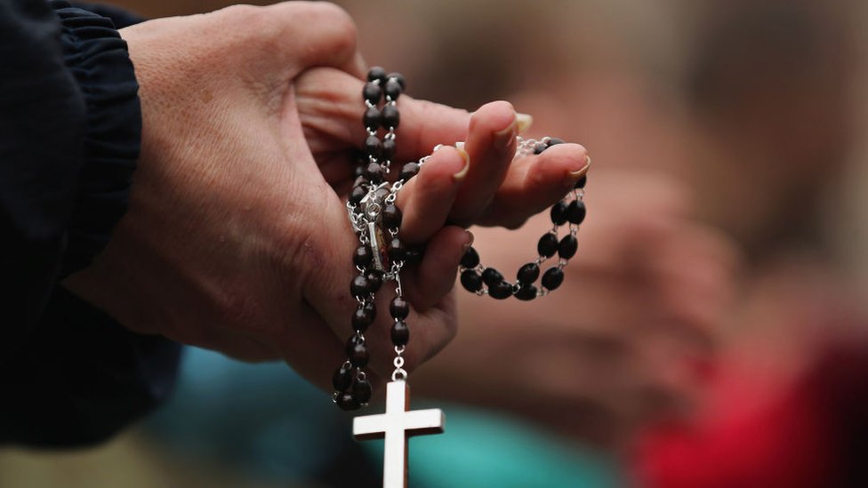 Persona rezando con un rosario en la mano.